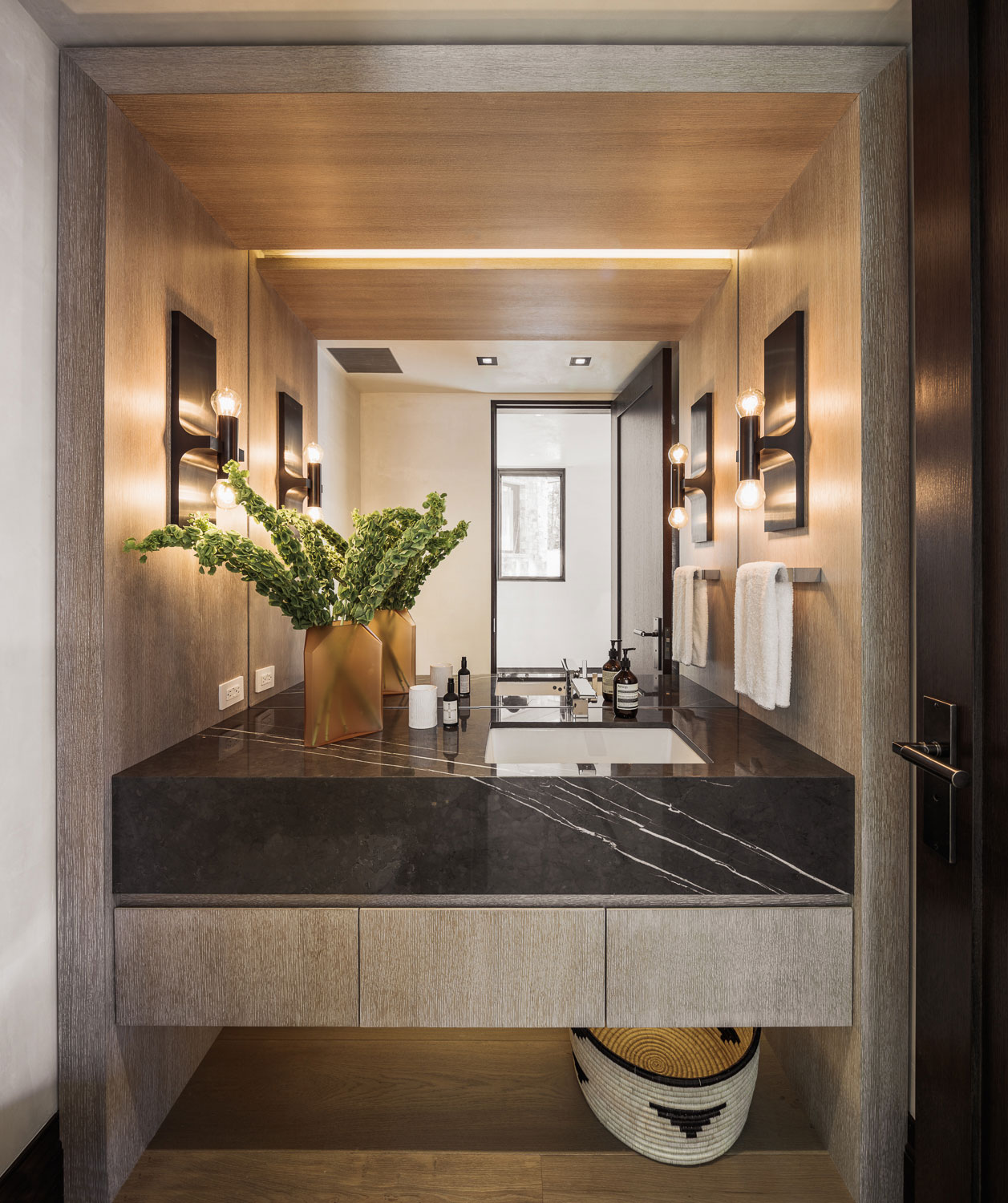 Red Mountain - Black marble vanity with grey wood grain architecture and black wall sconces. Interior...