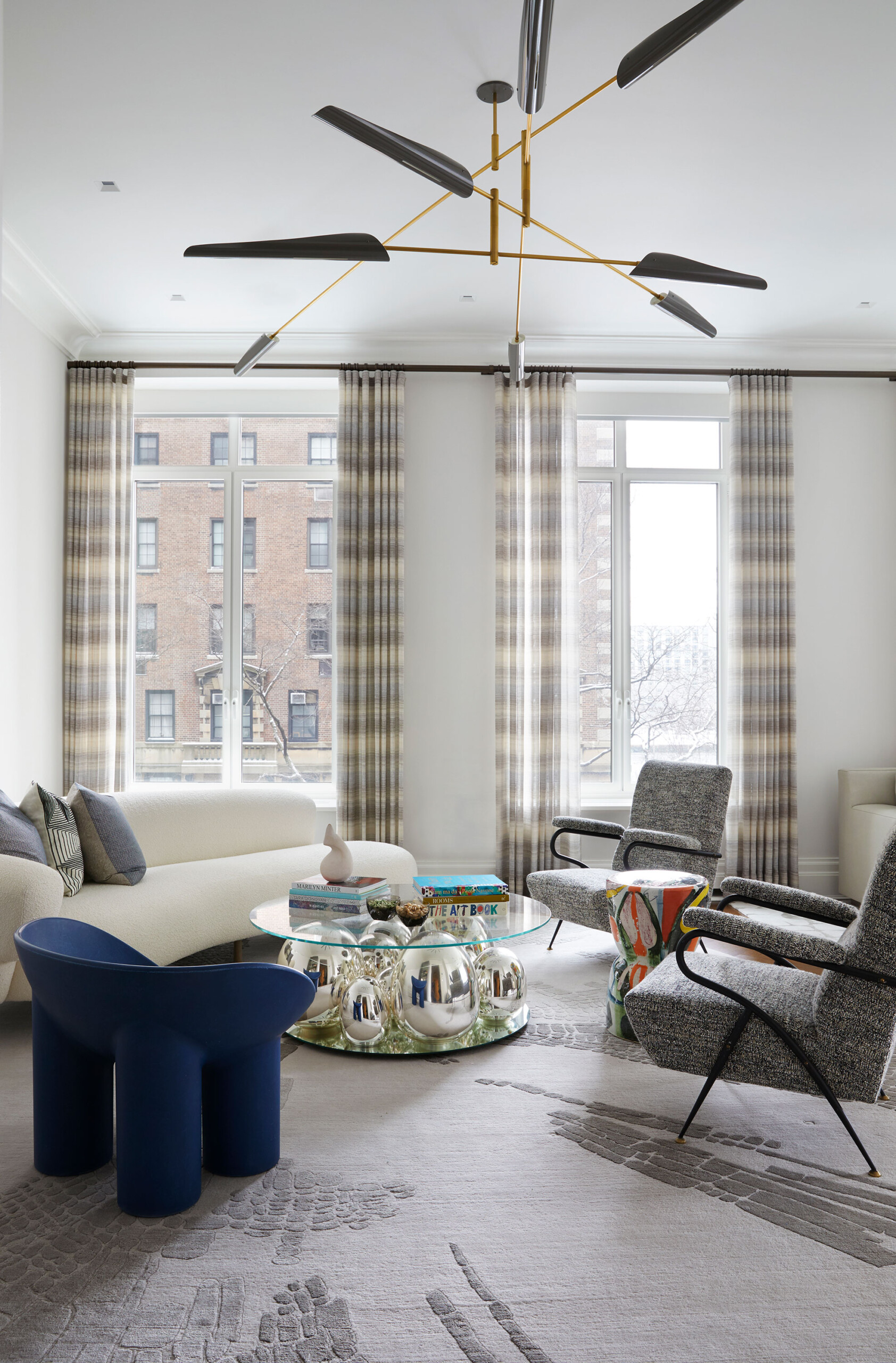 East End Avenue - Modern living room with rounded cream sofa, grey accent chairs, and navy blue...