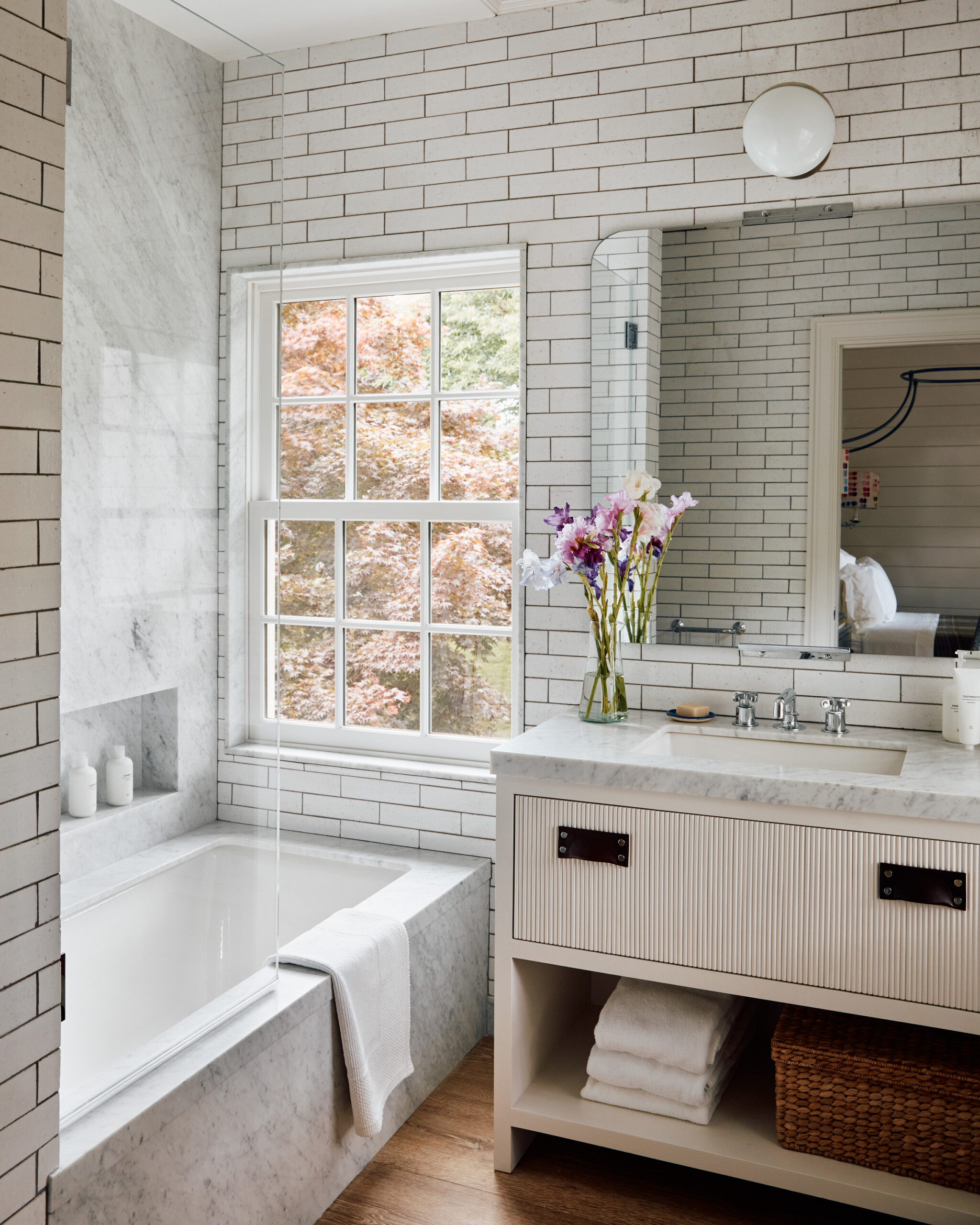 Hamptons Interior Design by Pembrooke & Ives. Bathroom with subway tiles, marble, and fluted wooden...