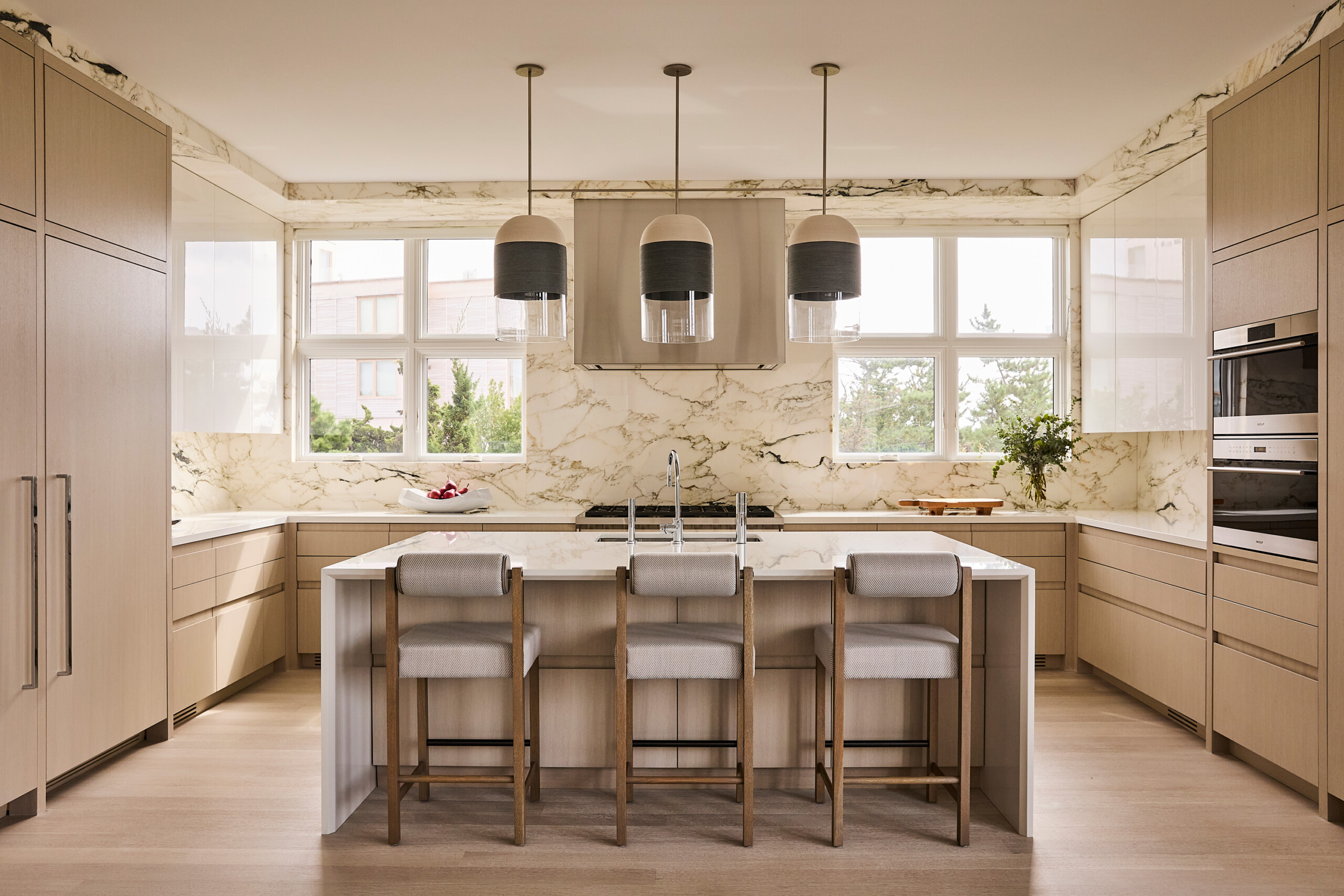 Hamptons Interior Design by Pembrooke & Ives. Kitchen with veined marble walls, glossy white cabinets,...