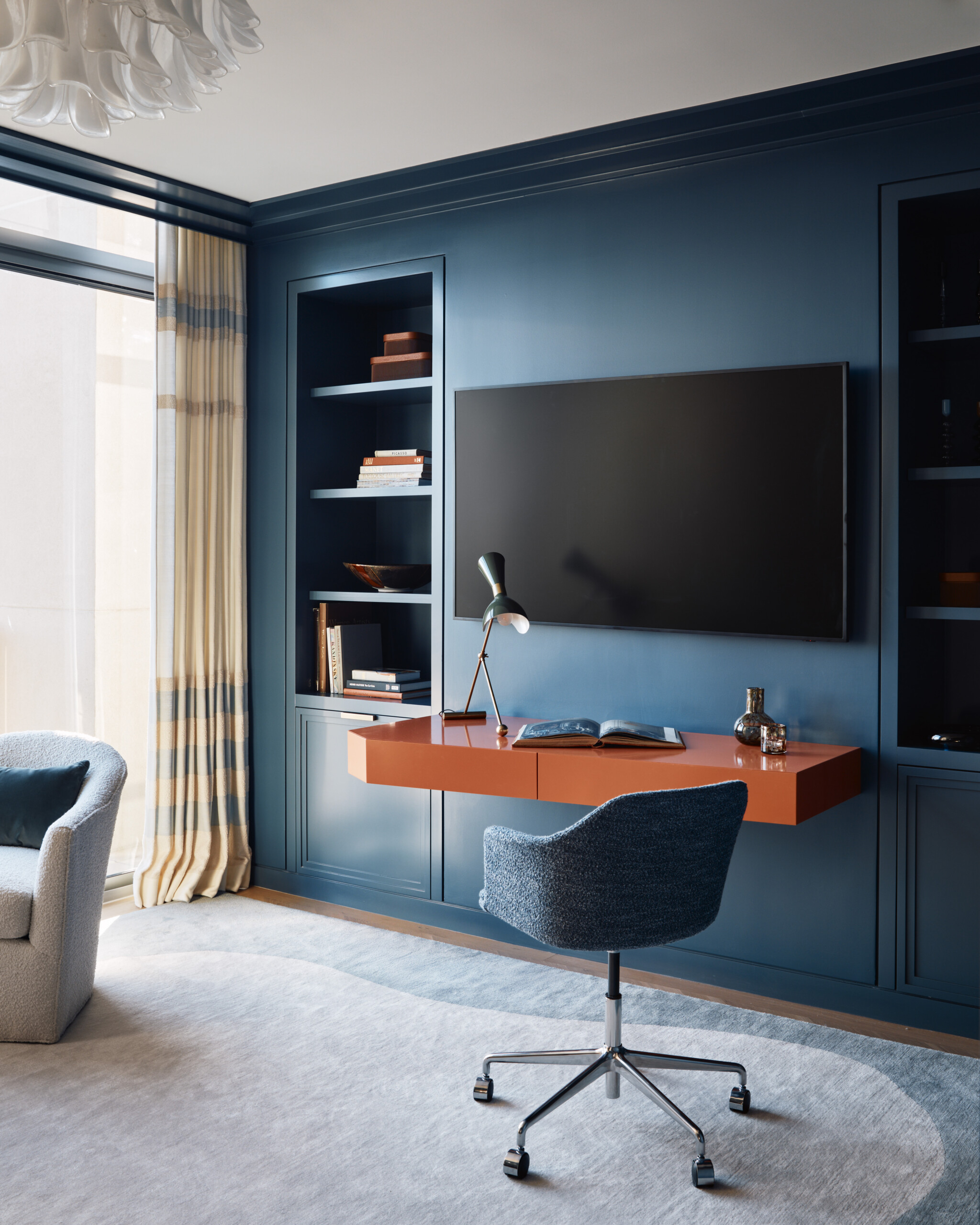 The Den features custom millwork painted in a deep teal blue, an orange lacquer cantilever desk...